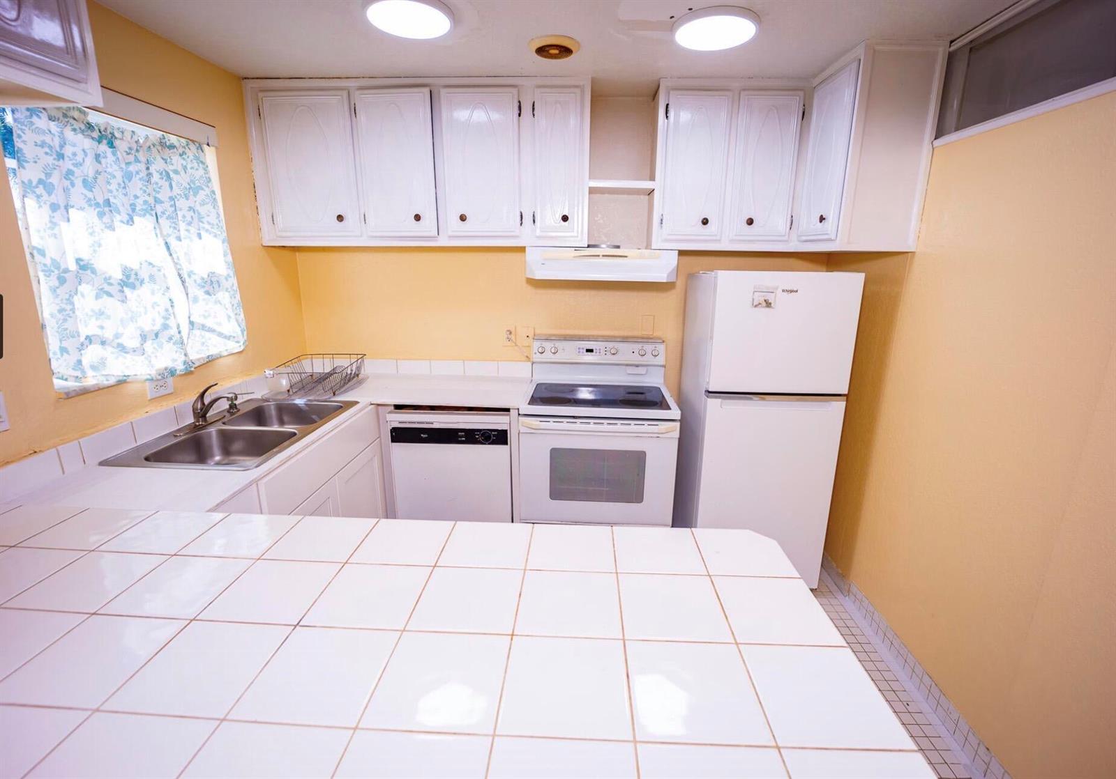 A kitchen features white cabinets, a tiled countertop, white appliances, and yellow walls — 3240 Ridge Hill Road # C, Boynton Beach FL 33435, BOYNTON BEACH, FL