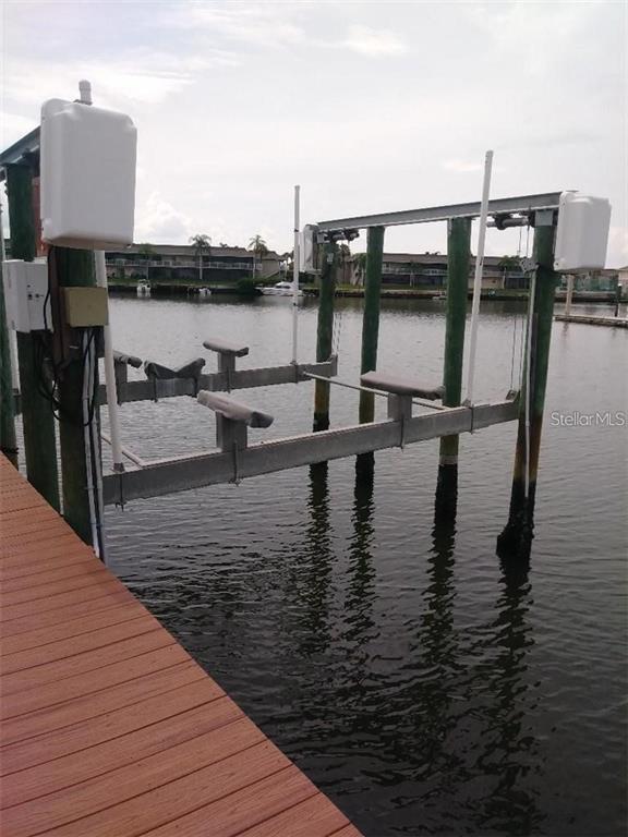 A boat lift with wooden bunks stands over a canal next to a wooden dock — 8720 COVE COURT, TAMPA, FL