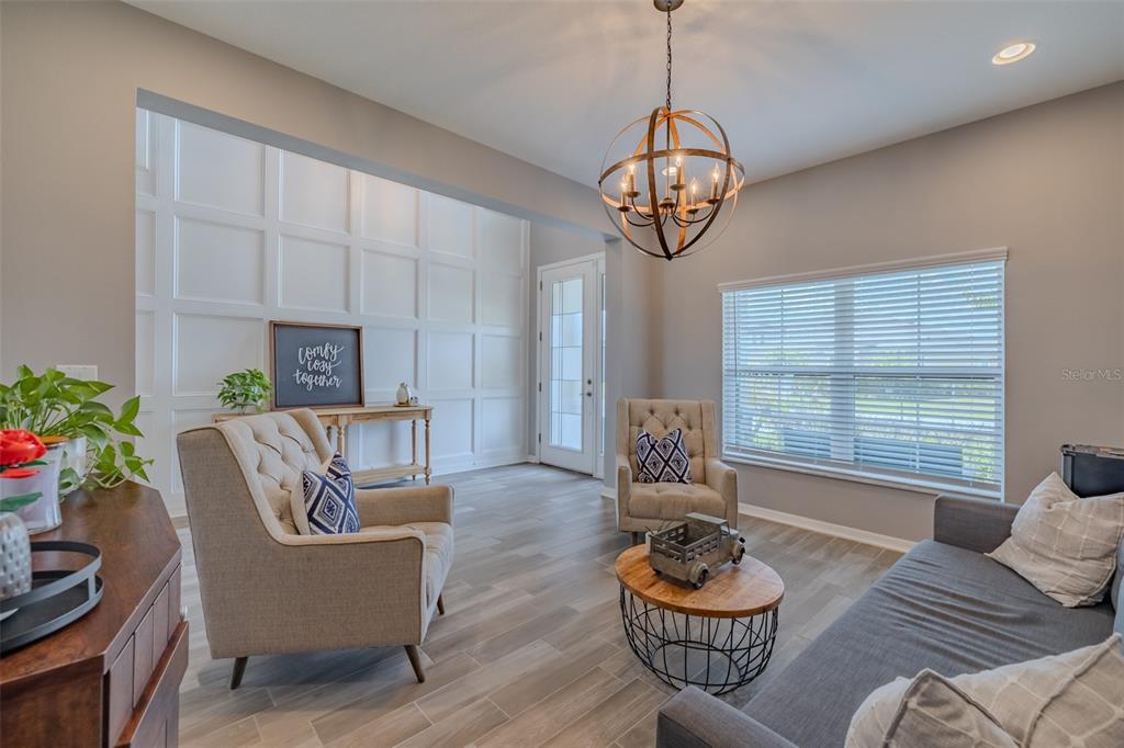 A living room features a grid-paneled accent wall, wood-look tile flooring, and a globe chandelier — 1686 CHERRY WALK ROAD, LUTZ, FL