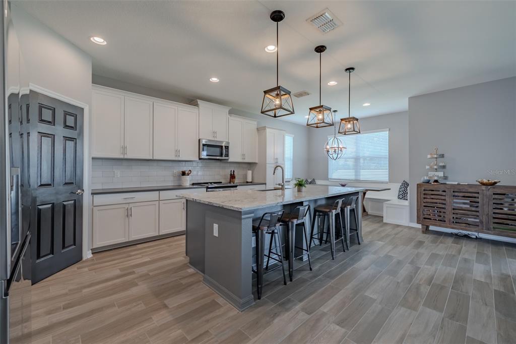 A modern kitchen features white cabinetry, a gray island with bar seating, and wood-look flooring — 1686 CHERRY WALK ROAD, LUTZ, FL