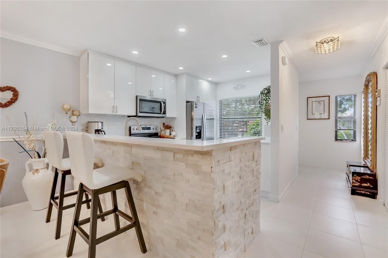 A modern kitchen features white cabinets, a stone-faced breakfast bar, and two white bar stools — 21364 Cypress Hammock Dr # 1H, Boca Raton FL 33428, BOCA RATON, FL