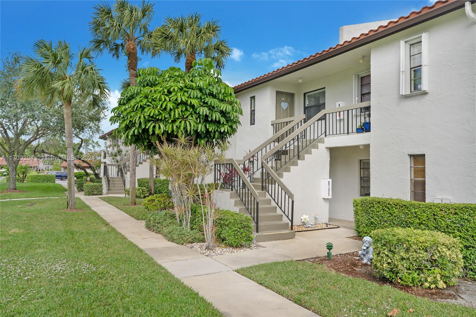 A two-story white stucco apartment building features exterior staircases and landscaped green space — 21364 Cypress Hammock Dr # 1H, Boca Raton FL 33428, BOCA RATON, FL