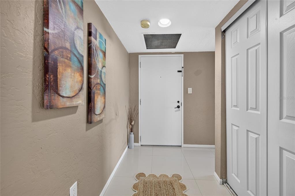 An entryway features beige walls, tiled floors, two abstract paintings, and a white front door — 2947 S ATLANTIC AVENUE UNIT 1706, DAYTONA BEACH, FL