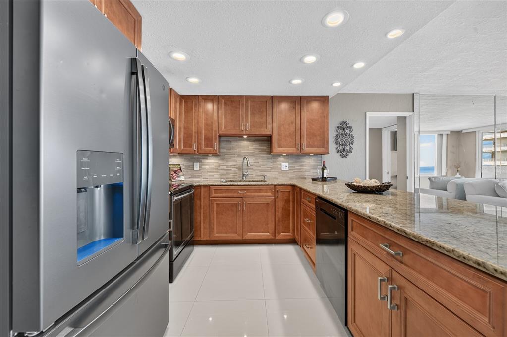 A kitchen features wood cabinets, granite countertops, stainless steel appliances, and light tile flooring — 2947 S ATLANTIC AVENUE UNIT 1706, DAYTONA BEACH, FL