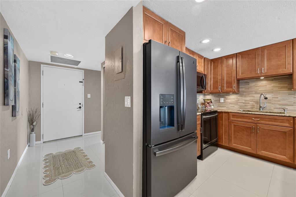 A kitchen with wood cabinets and stainless steel appliances sits beside an entryway with tile — 2947 S ATLANTIC AVENUE UNIT 1706, DAYTONA BEACH, FL