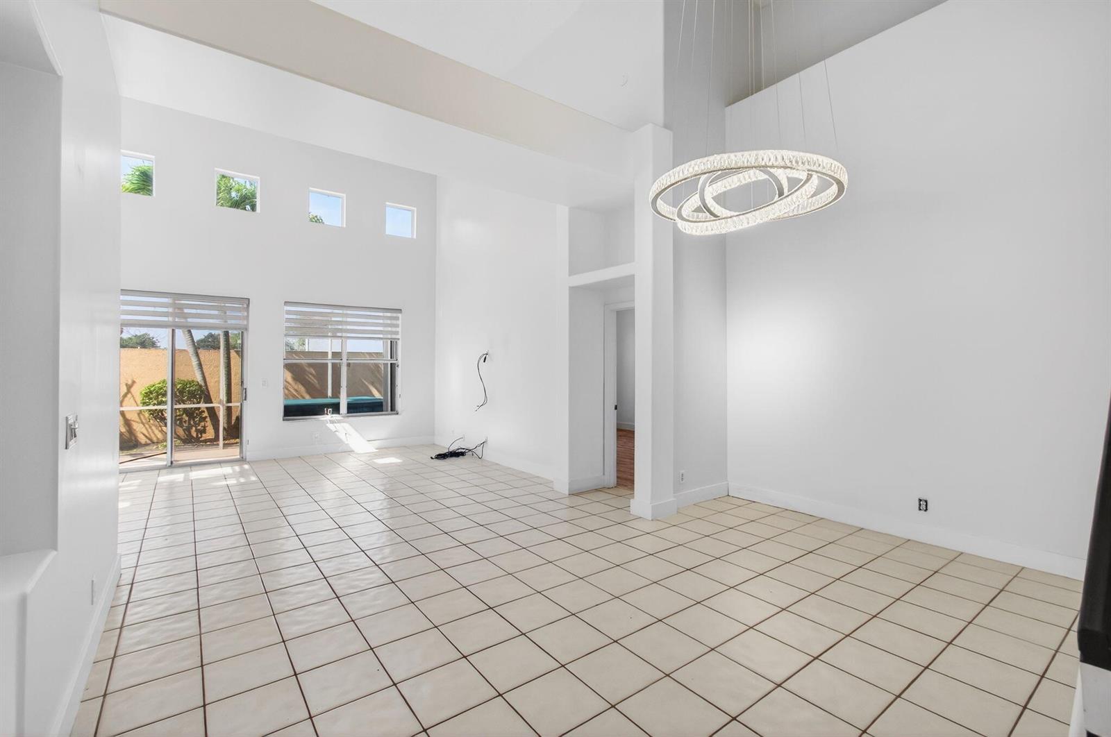 A bright, high-ceilinged living room features white walls, tiled flooring, and a modern circular chandelier — 7848 Travlers Tree Drive, Boca Raton FL 33433, BOCA RATON, FL