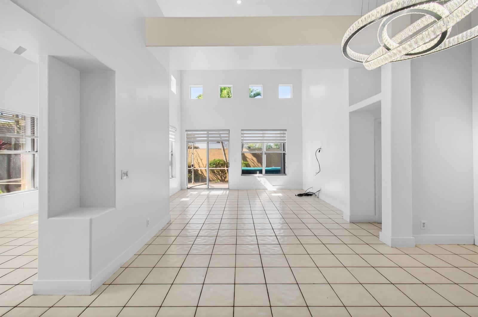 A bright, high-ceilinged living room features white walls, tiled floors, and a modern chandelier — 7848 Travlers Tree Drive, Boca Raton FL 33433, BOCA RATON, FL