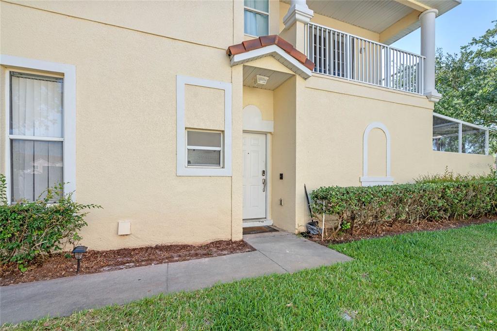 A beige two-story townhouse exterior features a white front door, a balcony, and landscaping — 4719 HEMINGWAY HOUSE STREET, KISSIMMEE, FL