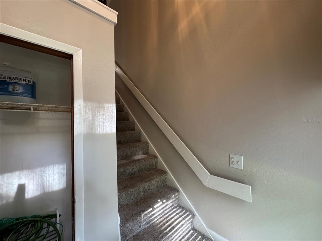 A carpeted staircase leads upward next to a storage closet containing a fuel container — 22 MID OAKS CIRCLE UNIT 22, PALM COAST, FL