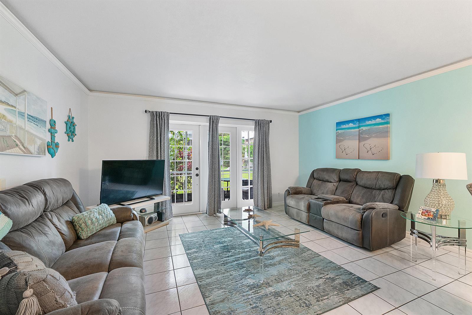 A living room features two gray reclining sofas, a glass coffee table, and tile flooring — 219 NE 14th Avenue # 107, Hallandale Beach FL 33009, HALLANDALE BEACH, FL