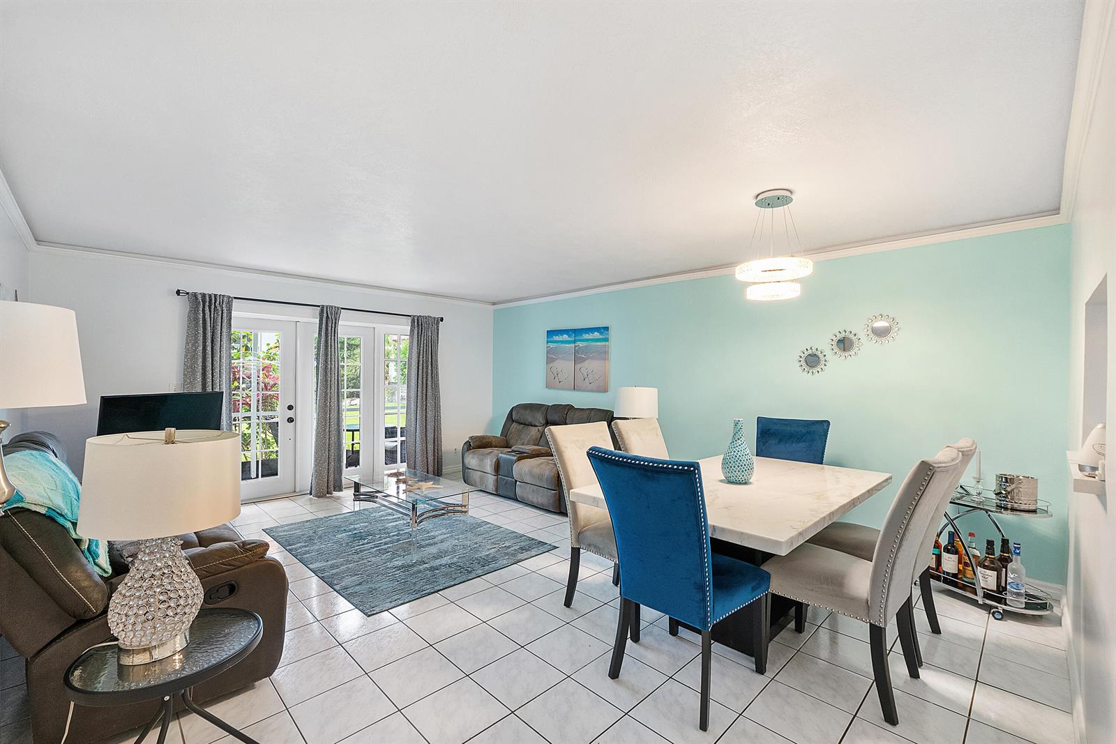 A living and dining room with tiled floors, a light blue accent wall, and patio doors — 219 NE 14th Avenue # 107, Hallandale Beach FL 33009, HALLANDALE BEACH, FL