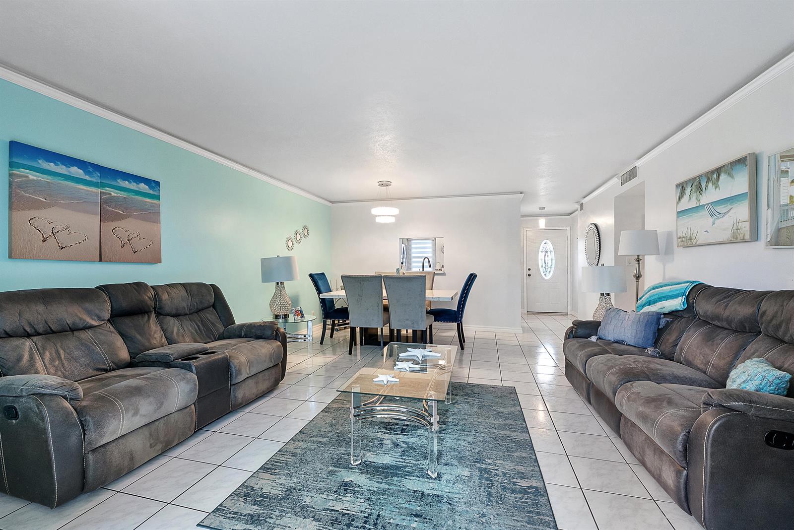 A living and dining area features gray reclining sofas, a glass coffee table, and tile flooring — 219 NE 14th Avenue # 107, Hallandale Beach FL 33009, HALLANDALE BEACH, FL