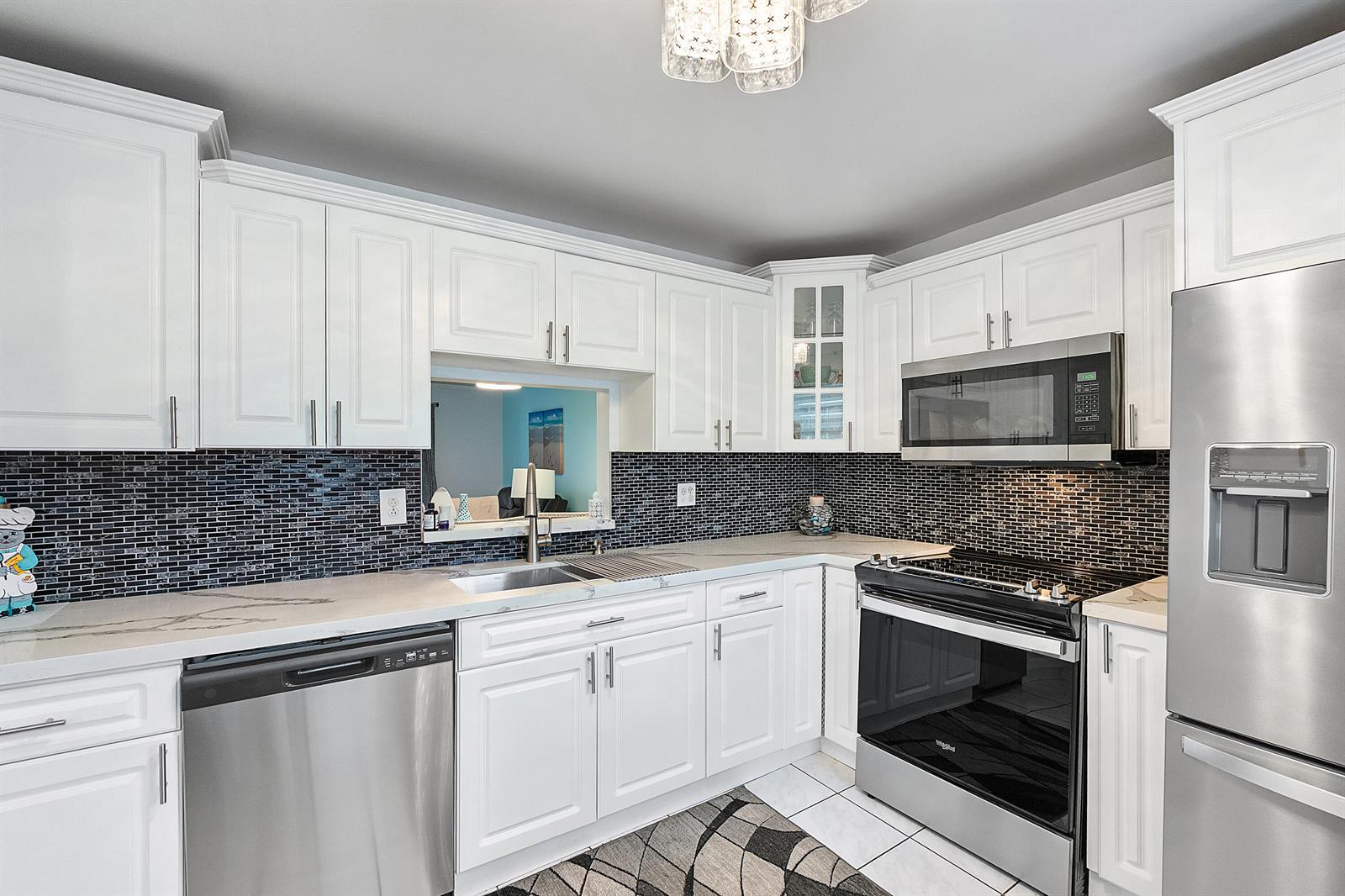 A kitchen features white cabinets, stainless steel appliances, and a dark glass tile backsplash — 219 NE 14th Avenue # 107, Hallandale Beach FL 33009, HALLANDALE BEACH, FL