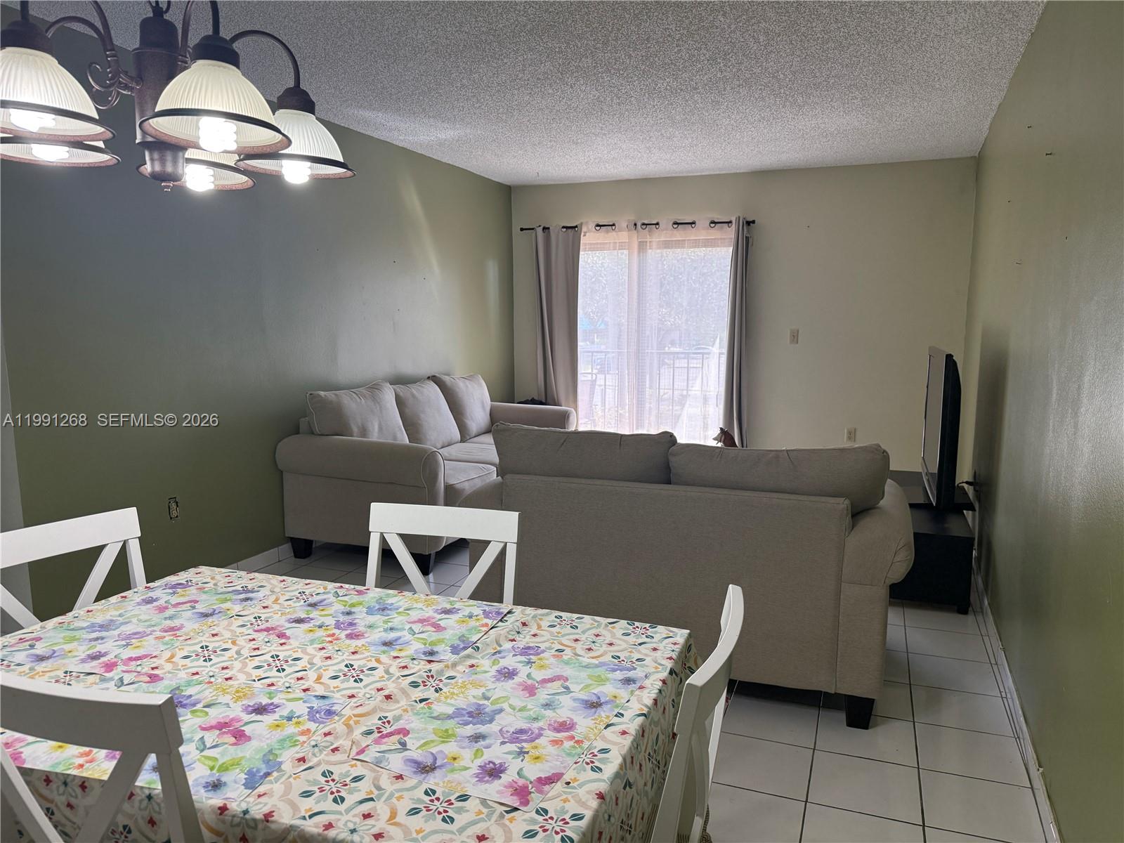 A dining area with a floral tablecloth sits adjacent to a living room with sofas — 1800 W 54th St # 108, Hialeah FL 33012, HIALEAH, FL