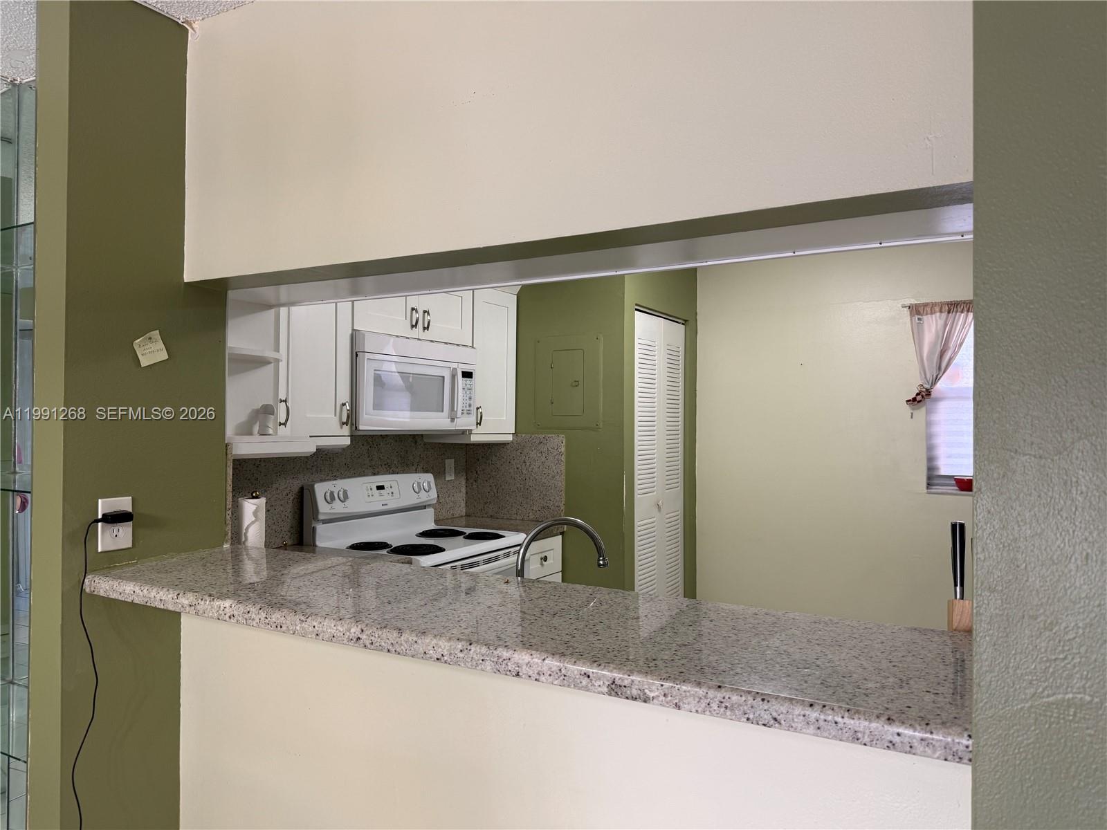 A kitchen features white cabinets, a granite countertop, and a pass-through window to another room — 1800 W 54th St # 108, Hialeah FL 33012, HIALEAH, FL
