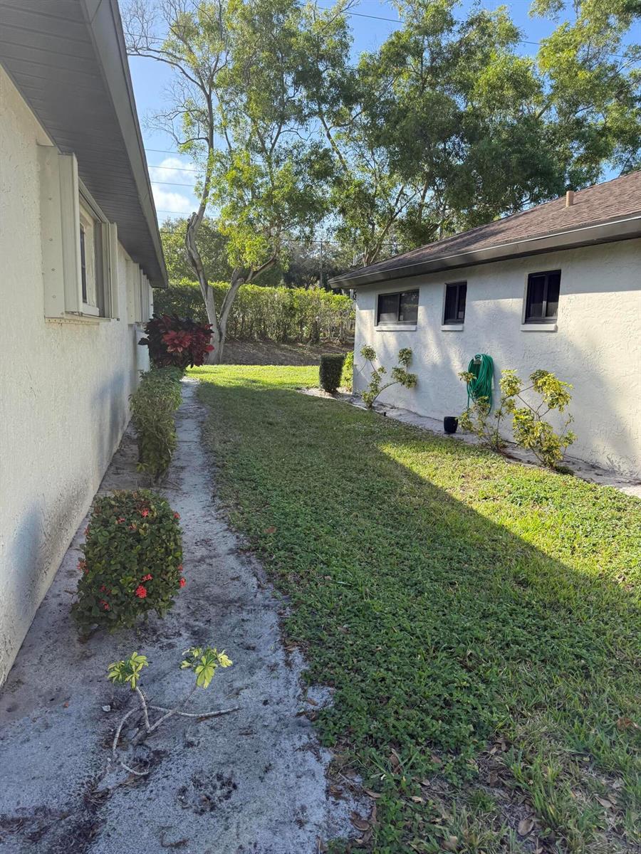 A narrow grassy yard sits between two stucco houses with small shrubs along the walls — 4948 Equestrian Circle # B, Boynton Beach FL 33436, BOYNTON BEACH, FL
