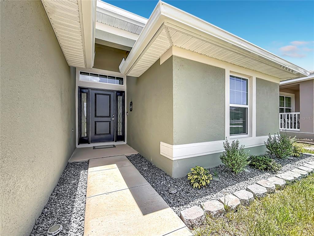 A concrete walkway leads to the dark front door of a house with green stucco — 5053 N TRIPLE EAGLE PATH, BEVERLY HILLS, FL