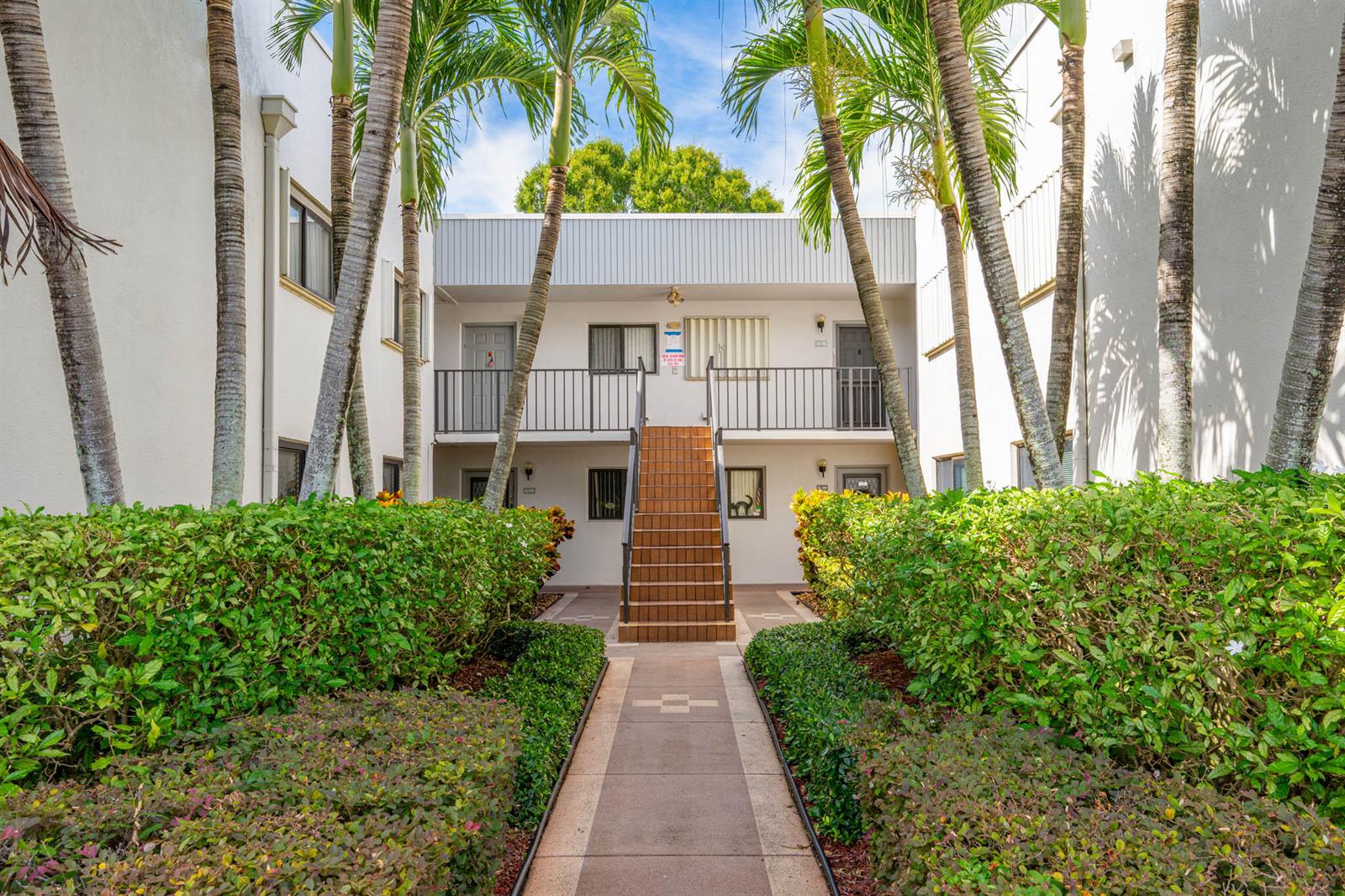A central staircase leads to the second-floor walkway of a two-story apartment building with landscaping — 15450 E Pembridge Avenue E # 192, Delray Beach FL 33484, DELRAY BEACH, FL