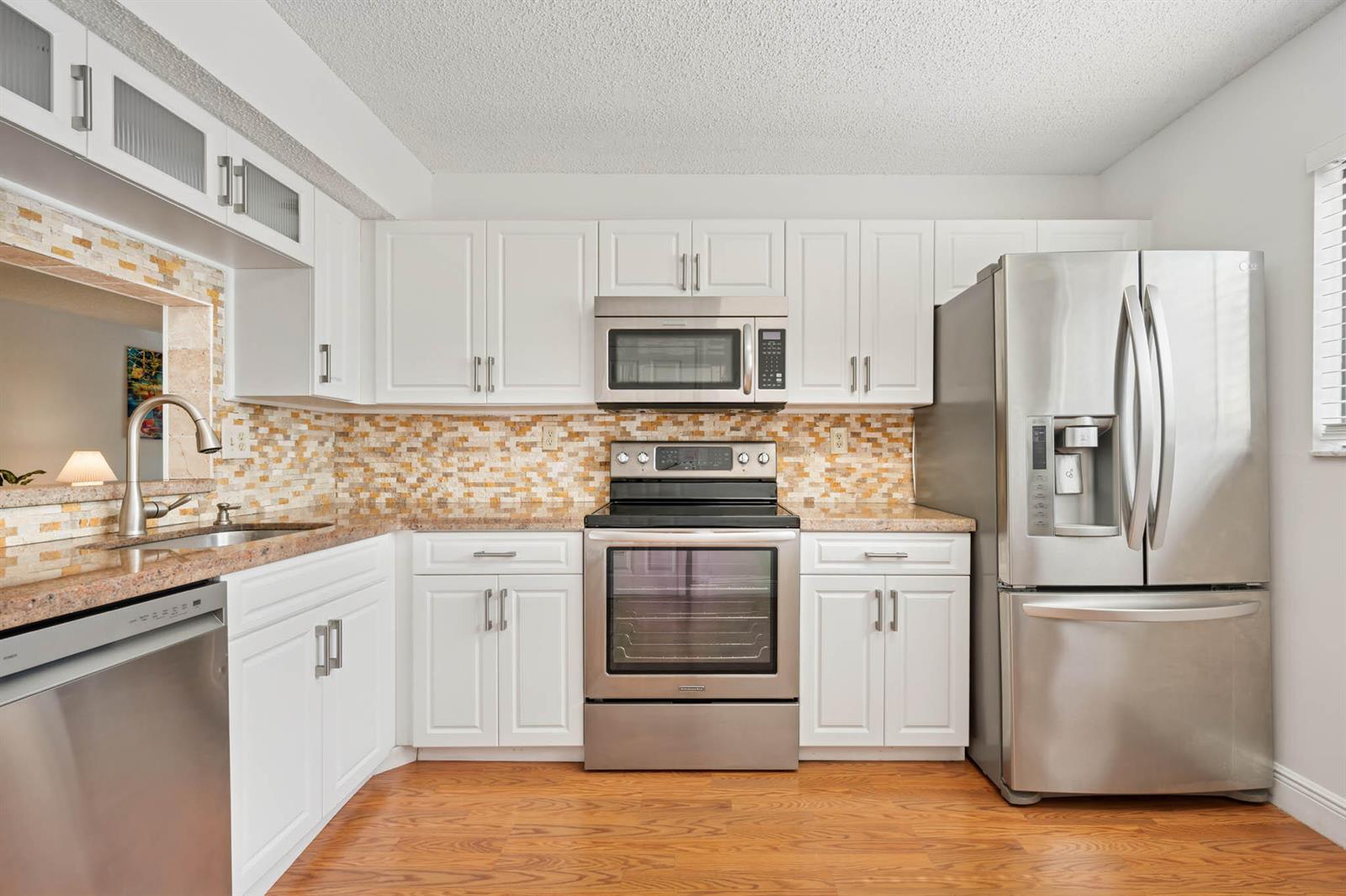 A kitchen features white cabinets, stainless steel appliances, a mosaic tile backsplash, and wood flooring — 15450 E Pembridge Avenue E # 192, Delray Beach FL 33484, DELRAY BEACH, FL