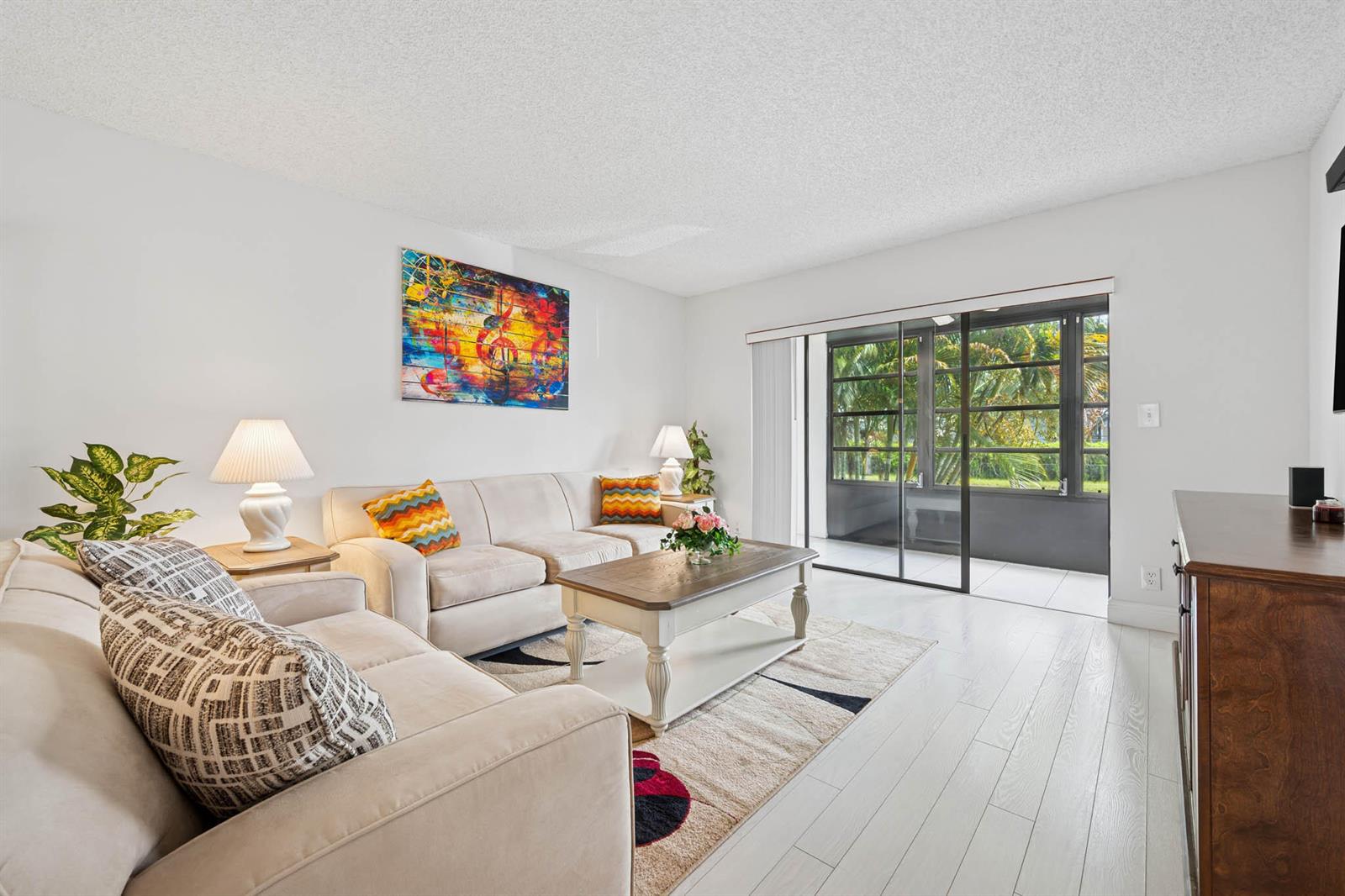 A living room features light-colored sofas, a coffee table, a patterned rug, and sliding glass doors — 15450 E Pembridge Avenue E # 192, Delray Beach FL 33484, DELRAY BEACH, FL