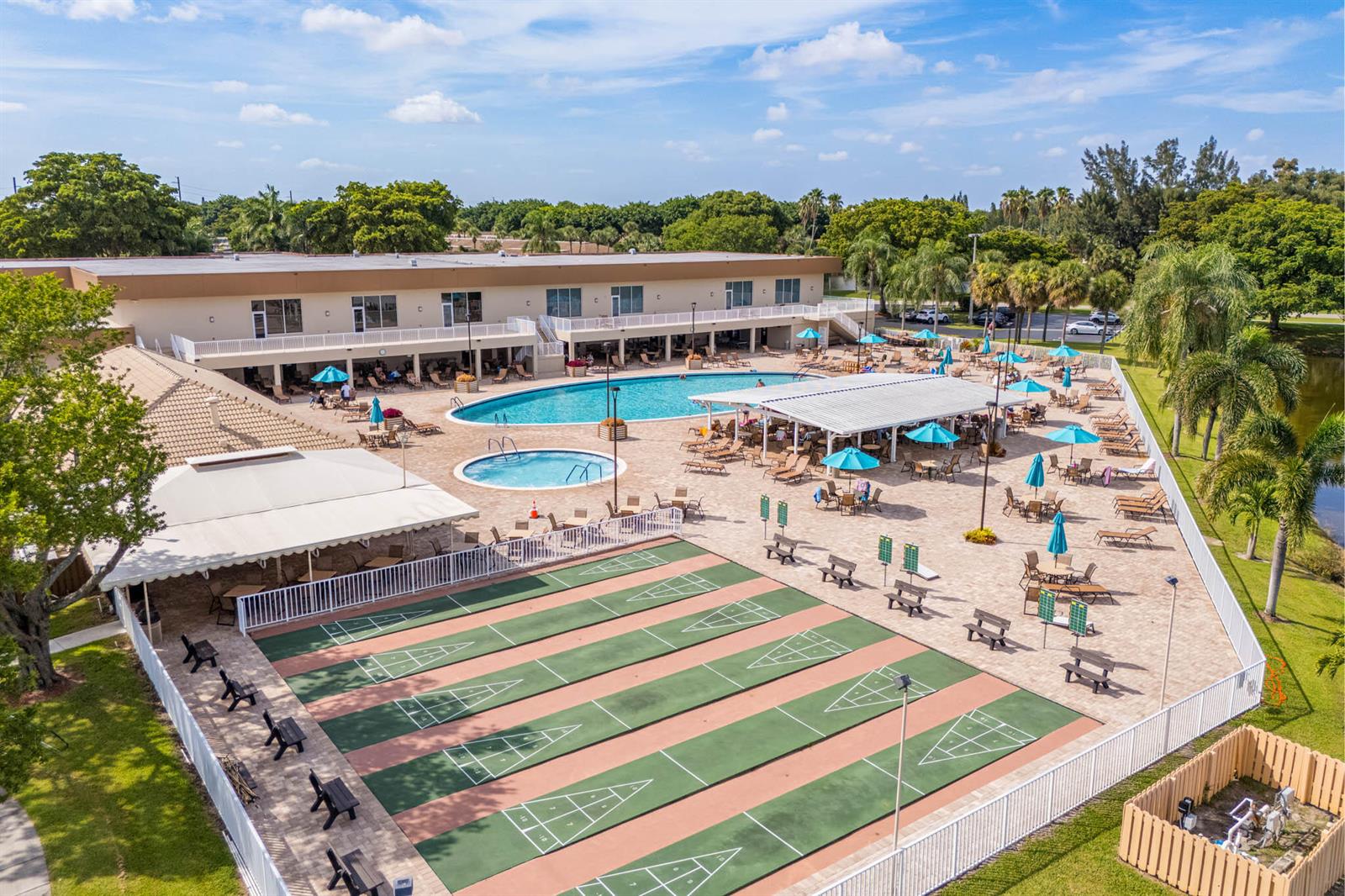 An aerial view shows a swimming pool, a smaller spa, and shuffleboard courts at a facility — 15450 E Pembridge Avenue E # 192, Delray Beach FL 33484, DELRAY BEACH, FL