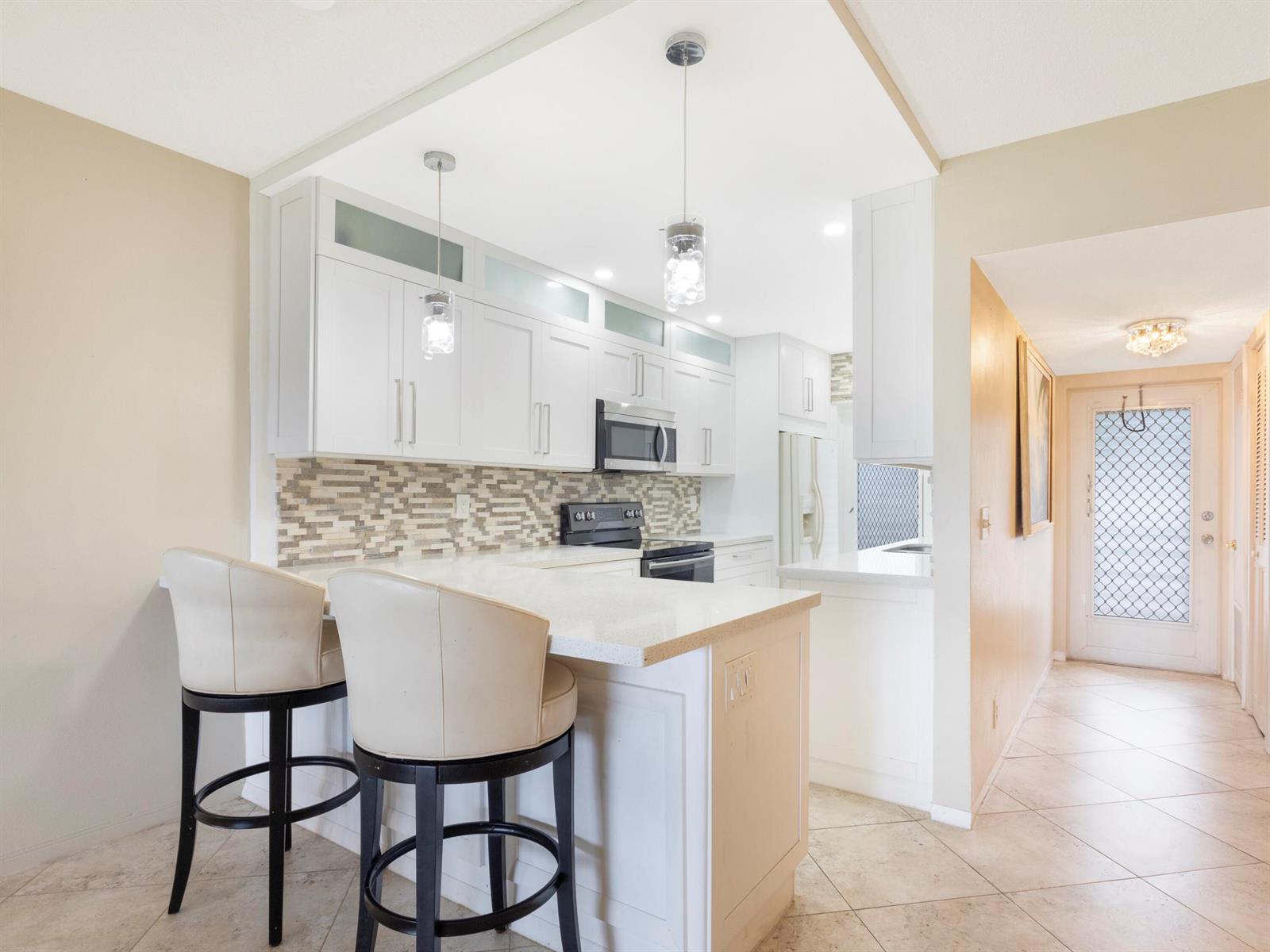 A kitchen with white cabinets, a breakfast bar with two stools, and tile flooring — 3421 Spanish Trail # 329, Delray Beach FL 33483, DELRAY BEACH, FL