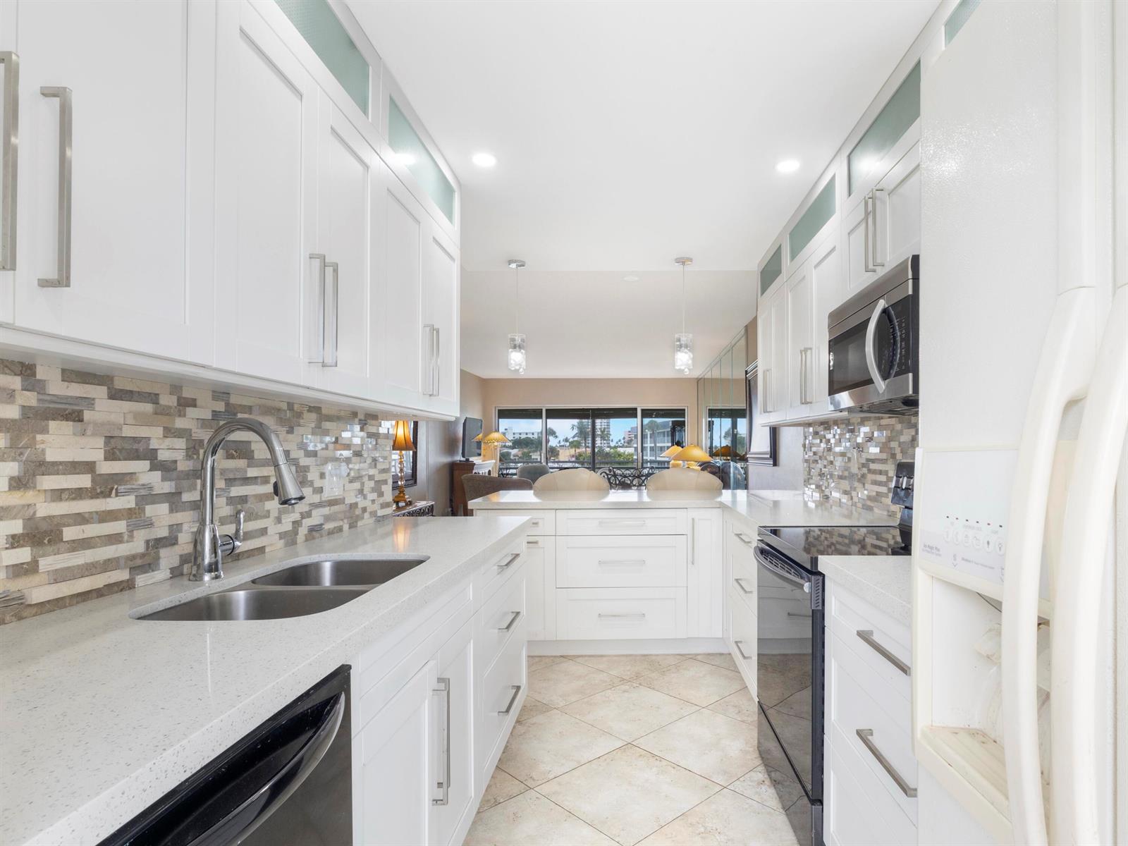 A galley kitchen features white cabinets, quartz countertops, a mosaic backsplash, and stainless steel appliances — 3421 Spanish Trail # 329, Delray Beach FL 33483, DELRAY BEACH, FL