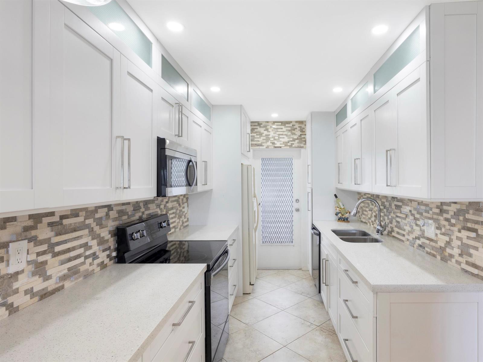 A galley kitchen features white cabinets, quartz countertops, a mosaic tile backsplash, and stainless appliances — 3421 Spanish Trail # 329, Delray Beach FL 33483, DELRAY BEACH, FL