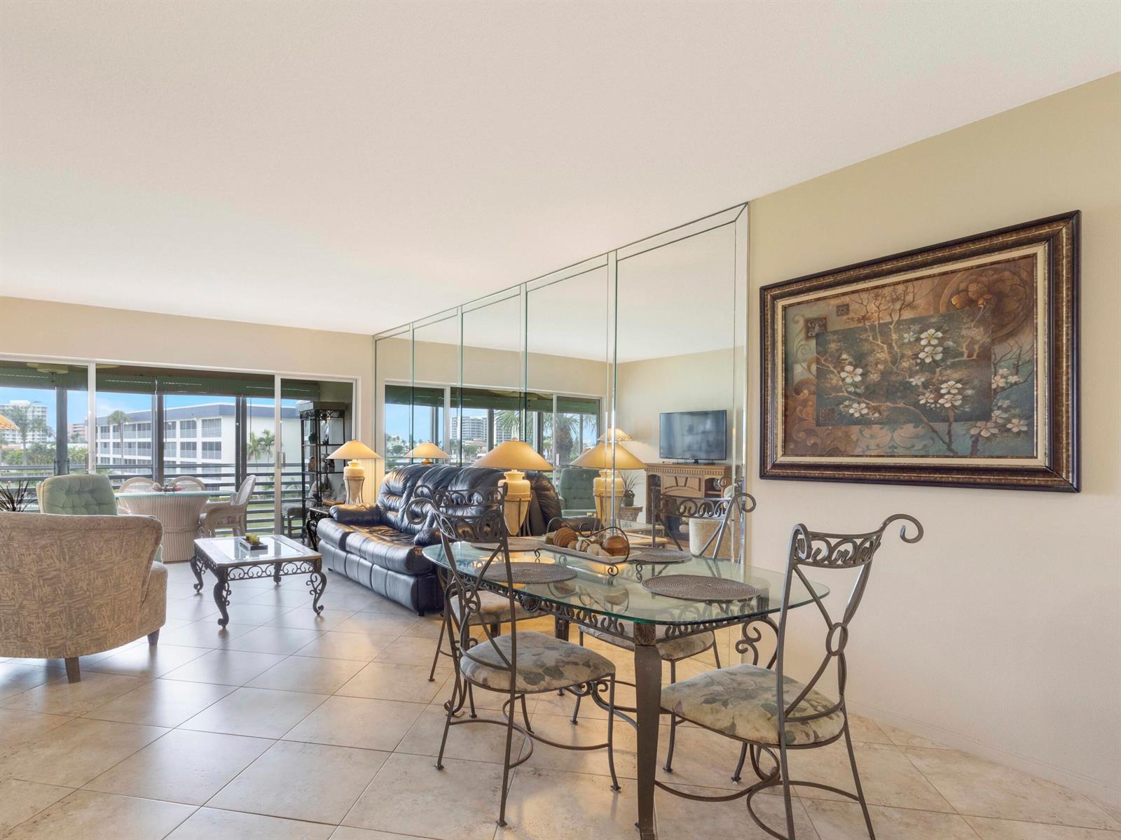 A dining area and living room with tiled floors, a mirrored wall, and balcony views — 3421 Spanish Trail # 329, Delray Beach FL 33483, DELRAY BEACH, FL