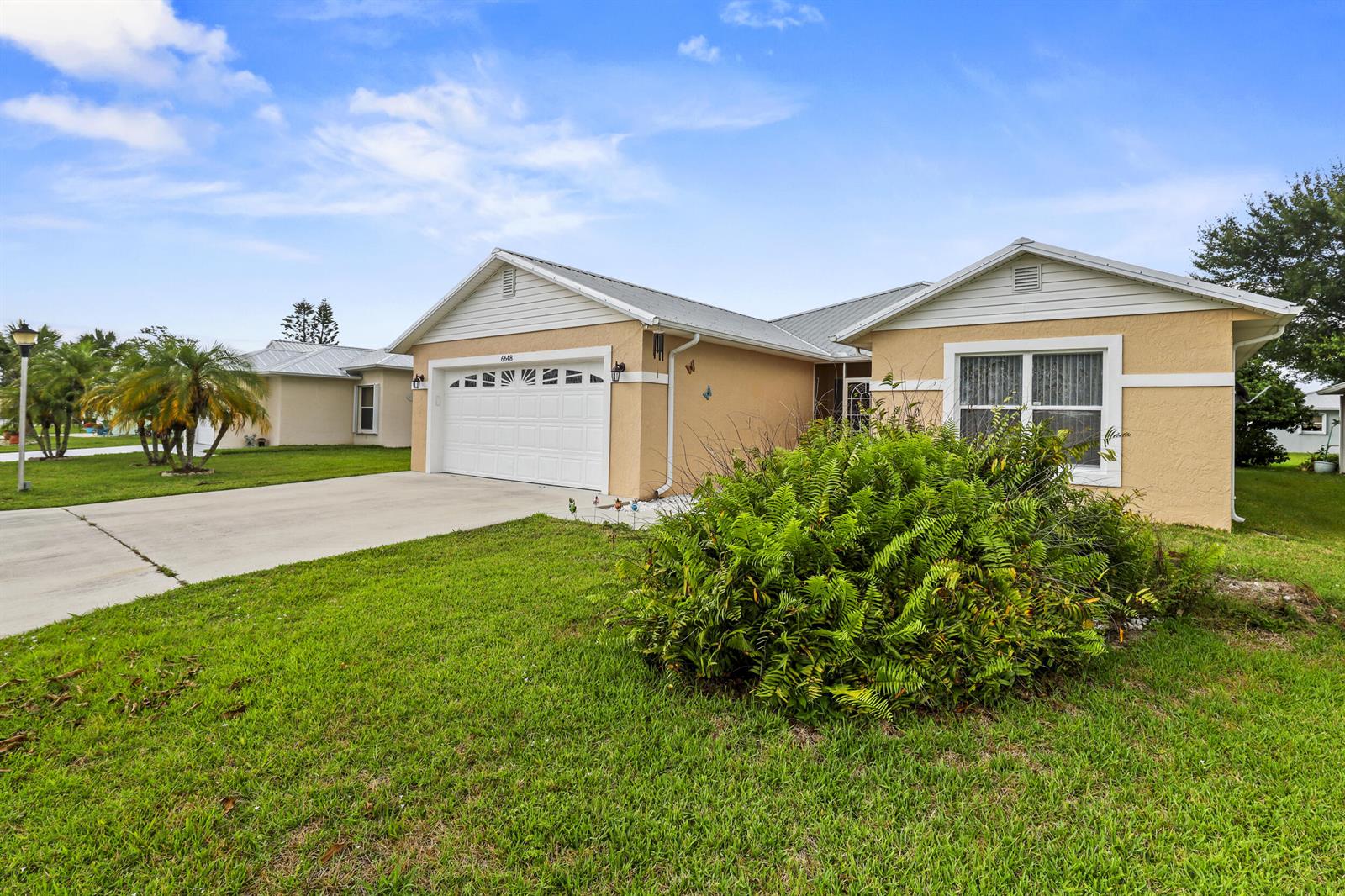 A single-story house with a tan exterior, white garage door, and a large front fern — 6648 Gaviota, Fort Pierce FL 34951, FORT PIERCE, FL