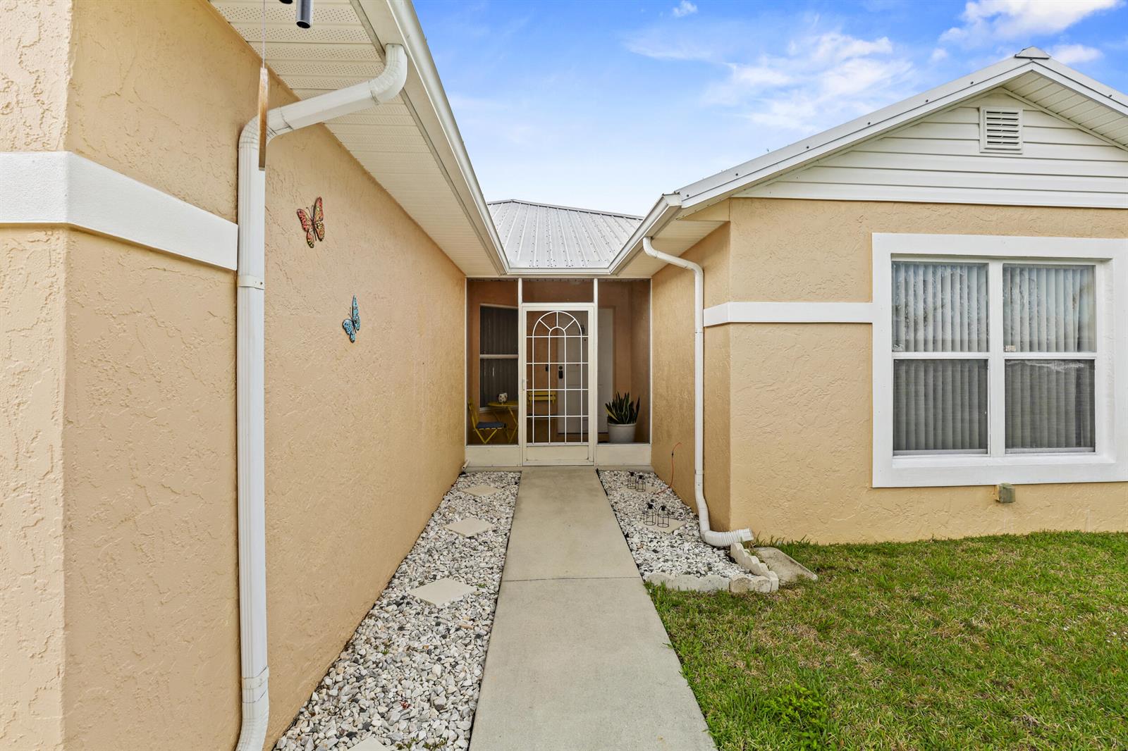 A concrete walkway leads to the screened front entryway of a beige stucco house — 6648 Gaviota, Fort Pierce FL 34951, FORT PIERCE, FL