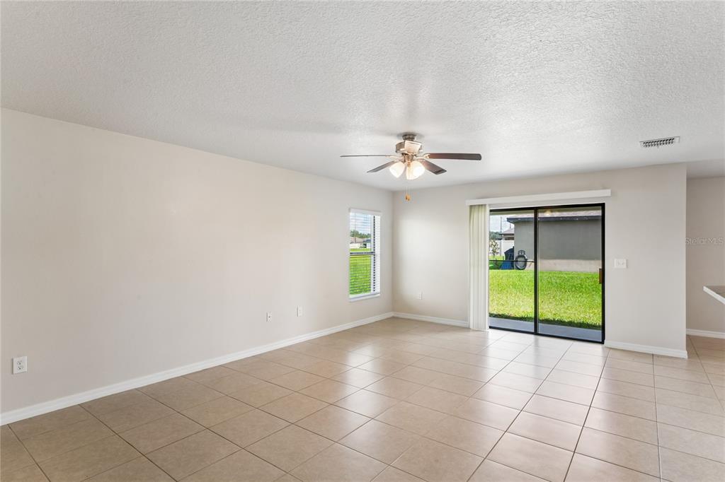 An empty living room with beige tile flooring, a ceiling fan, and sliding glass patio doors — 2403 CASPIAN DRIVE, LAKELAND, FL