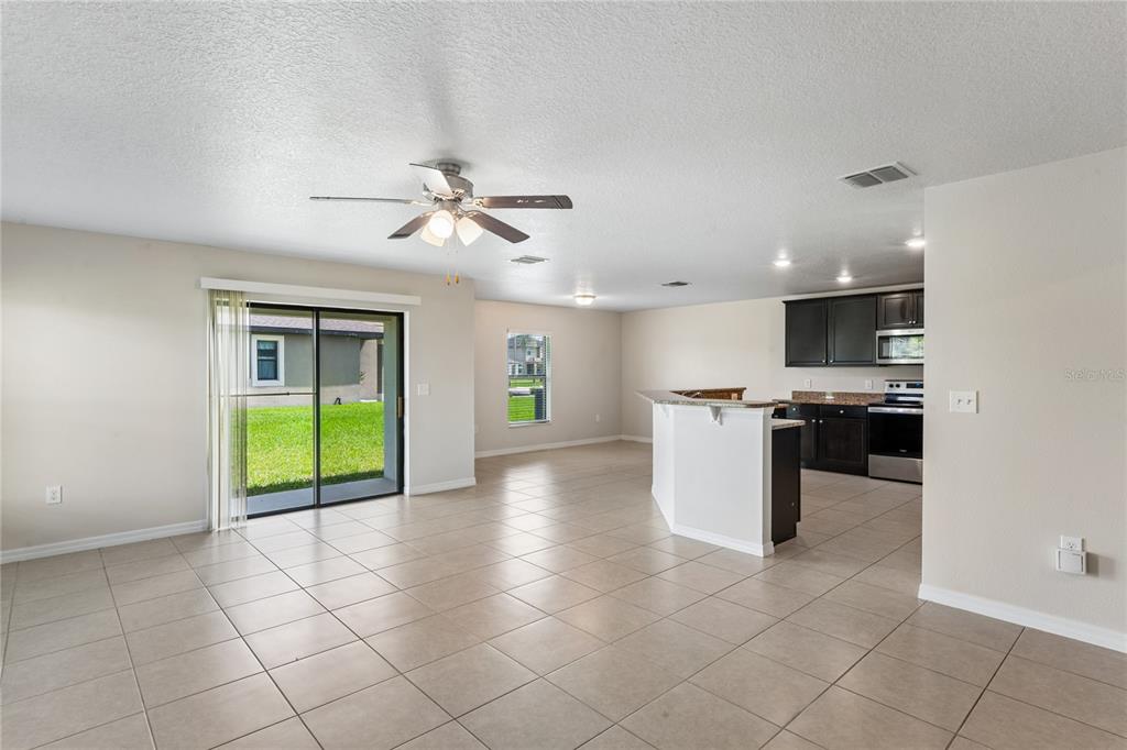 An open-concept living area features tile flooring, a ceiling fan, and an adjacent kitchen — 2403 CASPIAN DRIVE, LAKELAND, FL