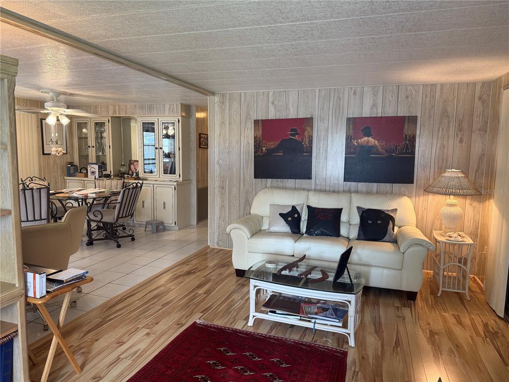 A living room with wood-paneled walls, a white sofa, and an adjacent dining area — 5640 FORSYTHIA ROAD, VENICE, FL