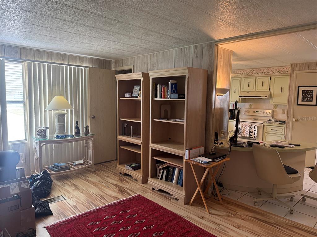 A living room with wood-paneled walls, two wooden bookshelves, and an open view into the kitchen — 5640 FORSYTHIA ROAD, VENICE, FL