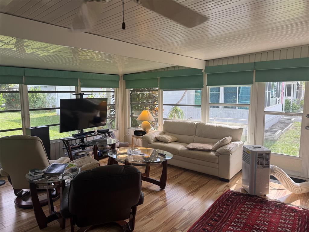 A sunroom features wood-look flooring, a white sofa, a television, and large windows — 5640 FORSYTHIA ROAD, VENICE, FL