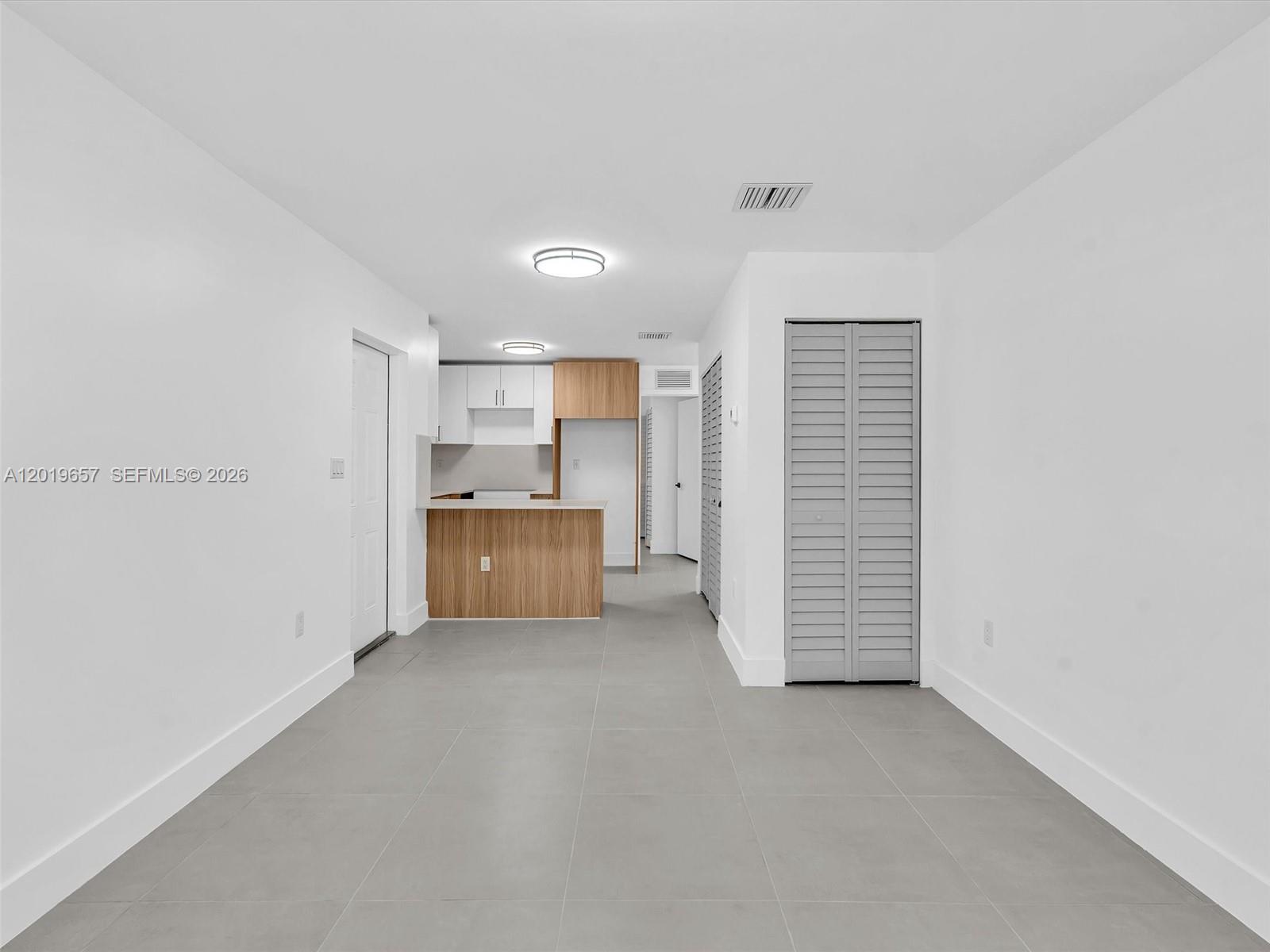 A minimalist room features gray tile flooring, white walls, and an open-concept kitchen area — 1840 NW 63rd St, Miami FL 33147, MIAMI, FL
