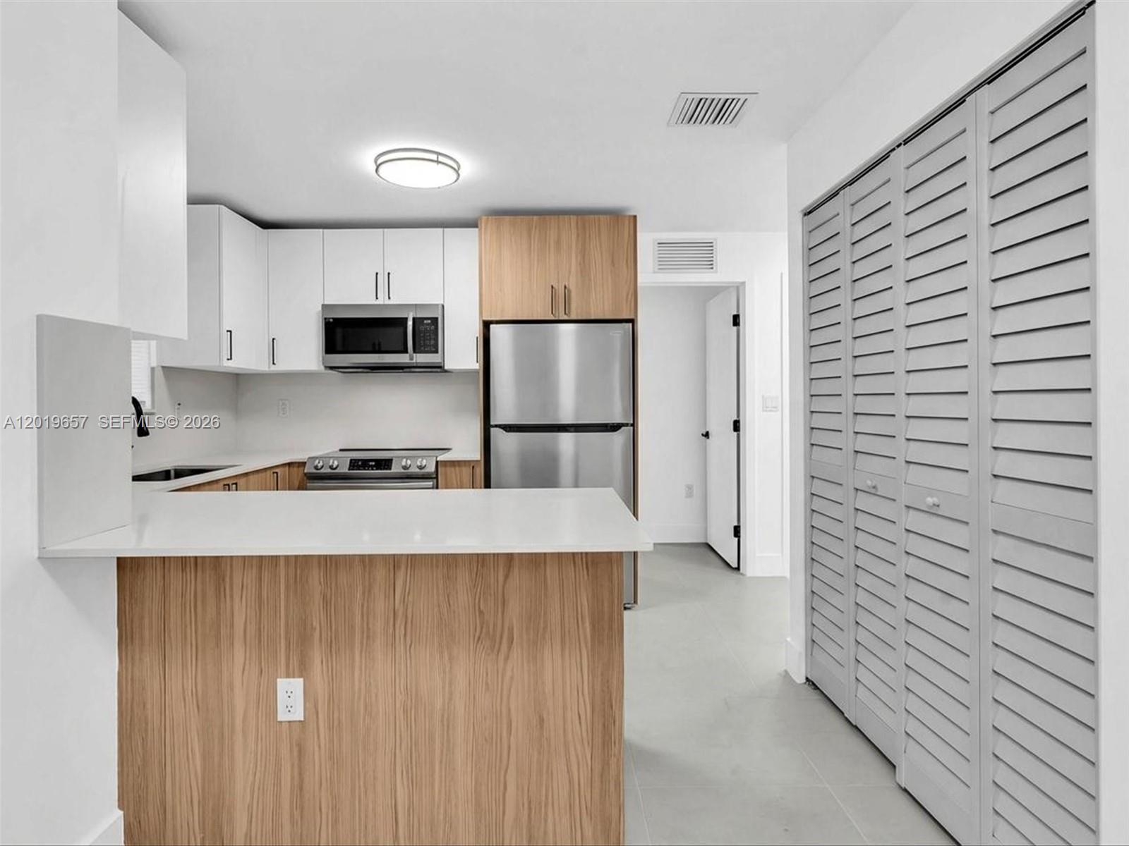 A kitchen features white and wood cabinets, stainless steel appliances, and a white countertop island — 1840 NW 63rd St, Miami FL 33147, MIAMI, FL