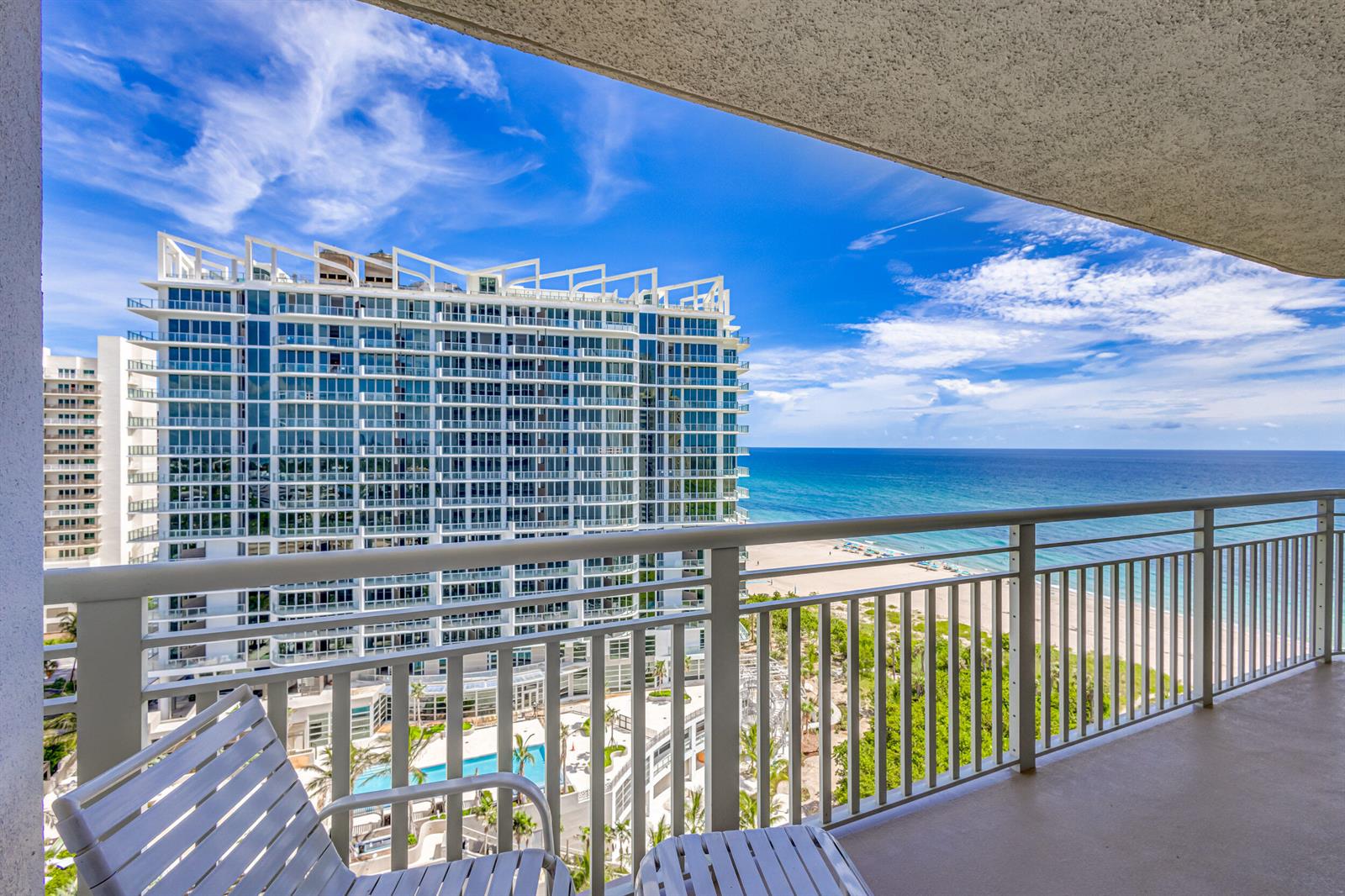 A balcony view overlooking a large white apartment building, a swimming pool, and the ocean — 3000 N Ocean Drive # B, Singer Island FL 33404, SINGER ISLAND, FL
