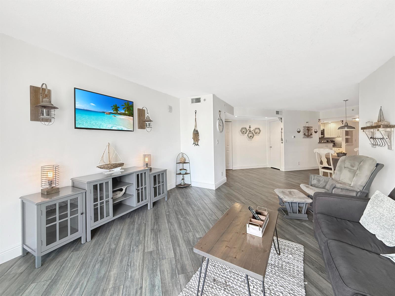 A living room features gray wood-look flooring, a television, and coastal-themed decor — 3000 N Ocean Drive # B, Singer Island FL 33404, SINGER ISLAND, FL