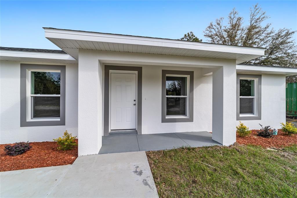 A white house exterior features a covered front porch, a white door, and gray trim — 146 SW TREE TOP ROAD, DUNNELLON, FL