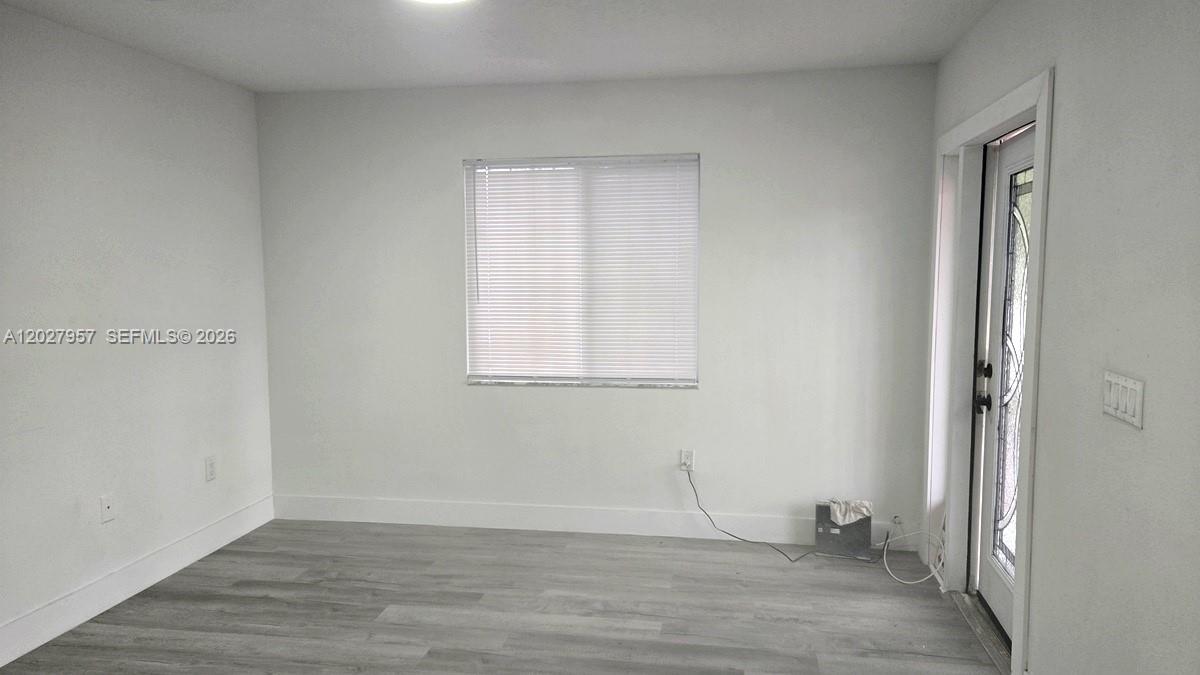 A room with light gray walls, wood-look flooring, a window with blinds, and a glass-paneled door — 4952 NW 21st Ave # 0, Miami FL 33142, MIAMI, FL