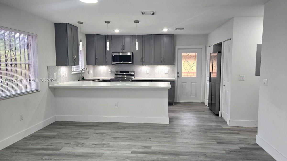 A modern kitchen features gray cabinets, white countertops, and light wood-look flooring — 4952 NW 21st Ave # 0, Miami FL 33142, MIAMI, FL