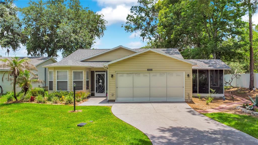 A single-story house with beige siding, a two-car garage, and a screened-in side porch — 32222 SUMMERTREE CIRCLE, LEESBURG, FL