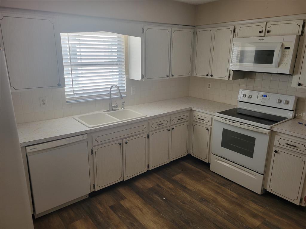A kitchen features white cabinets, white appliances, a double sink, and wood-look flooring — 7530 JUDITH CRESCENT CRESCENT, PORT RICHEY, FL