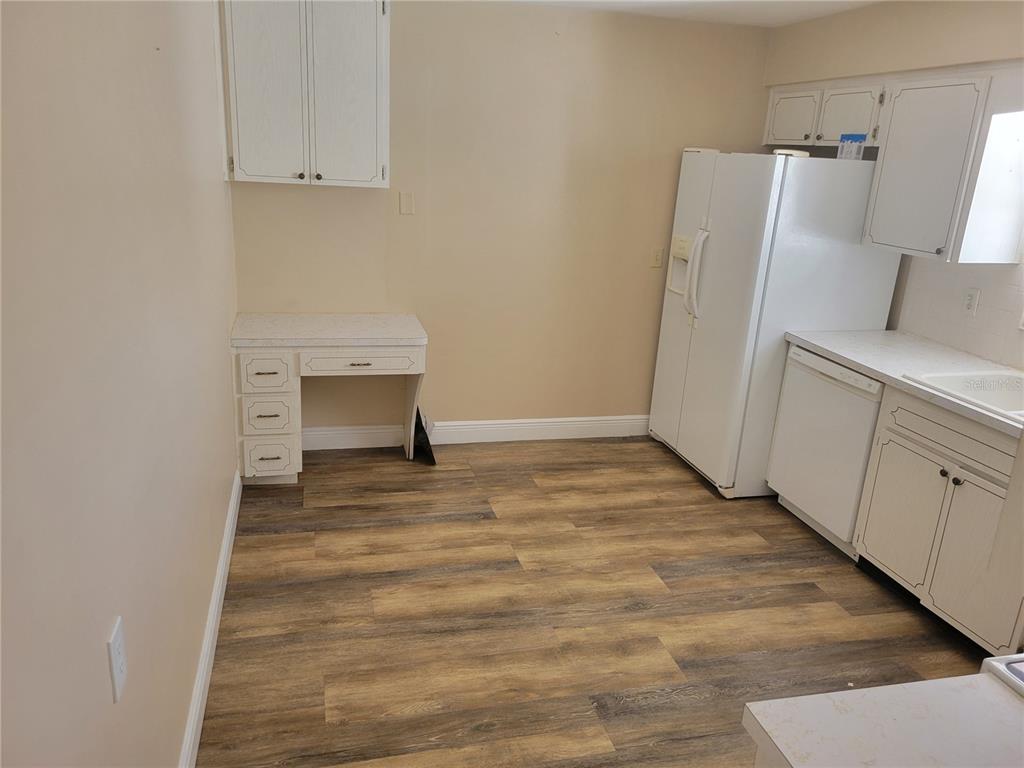 A kitchen features white cabinetry, a built-in desk, a white refrigerator, and wood-look flooring — 7530 JUDITH CRESCENT CRESCENT, PORT RICHEY, FL