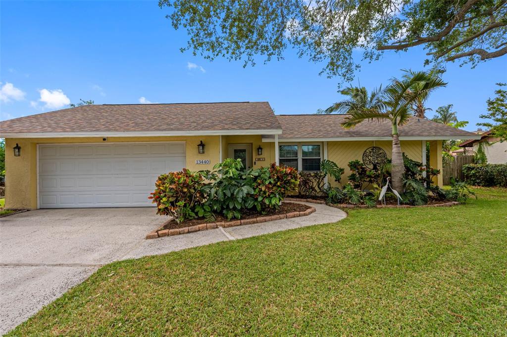 A single-story yellow house with a two-car garage, shingled roof, and landscaped front yard — 13440 RUSTIC PINES BOULEVARD S, SEMINOLE, FL