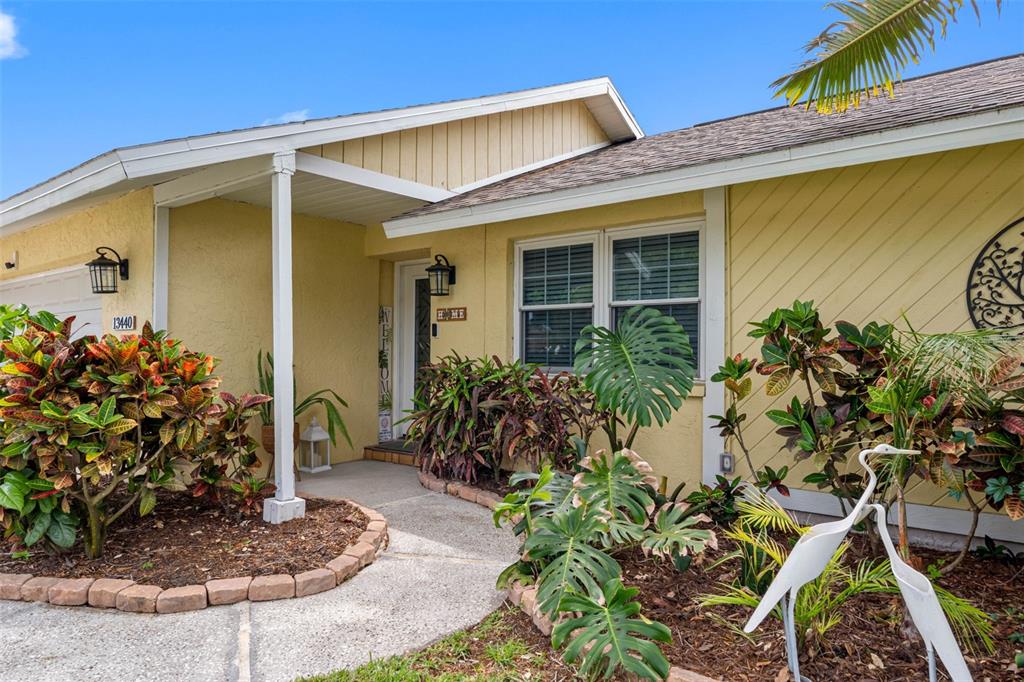 The exterior of a yellow house features a front walkway, landscaping, and a covered entryway — 13440 RUSTIC PINES BOULEVARD S, SEMINOLE, FL