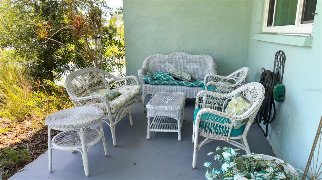 A covered patio features white wicker furniture set against a light blue exterior wall — 2215 ALVARADO LANE, SARASOTA, FL