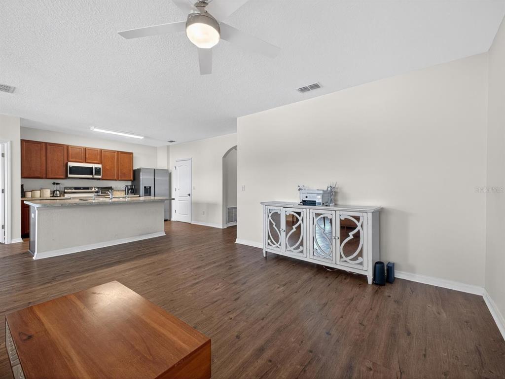 An open-concept living area features wood-look flooring, a kitchen with a breakfast bar, and cabinetry — 16701 BROADFORD LANE, CLERMONT, FL